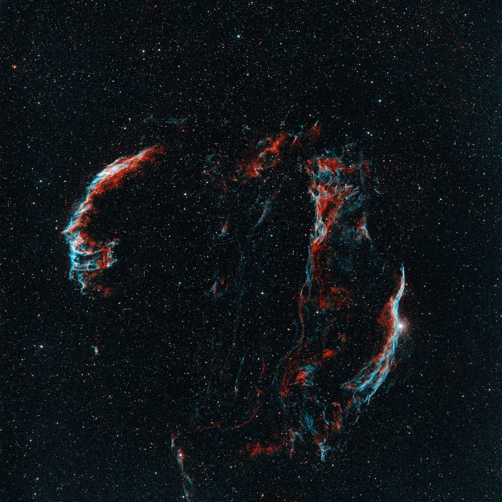 A dark field crowded with small stars, crossed by a broken ring of glowing filaments: a red and blue arc on the left, a tangle of red wisps at the top middle, and a long red and blue sweep on the right passing a bright white star.