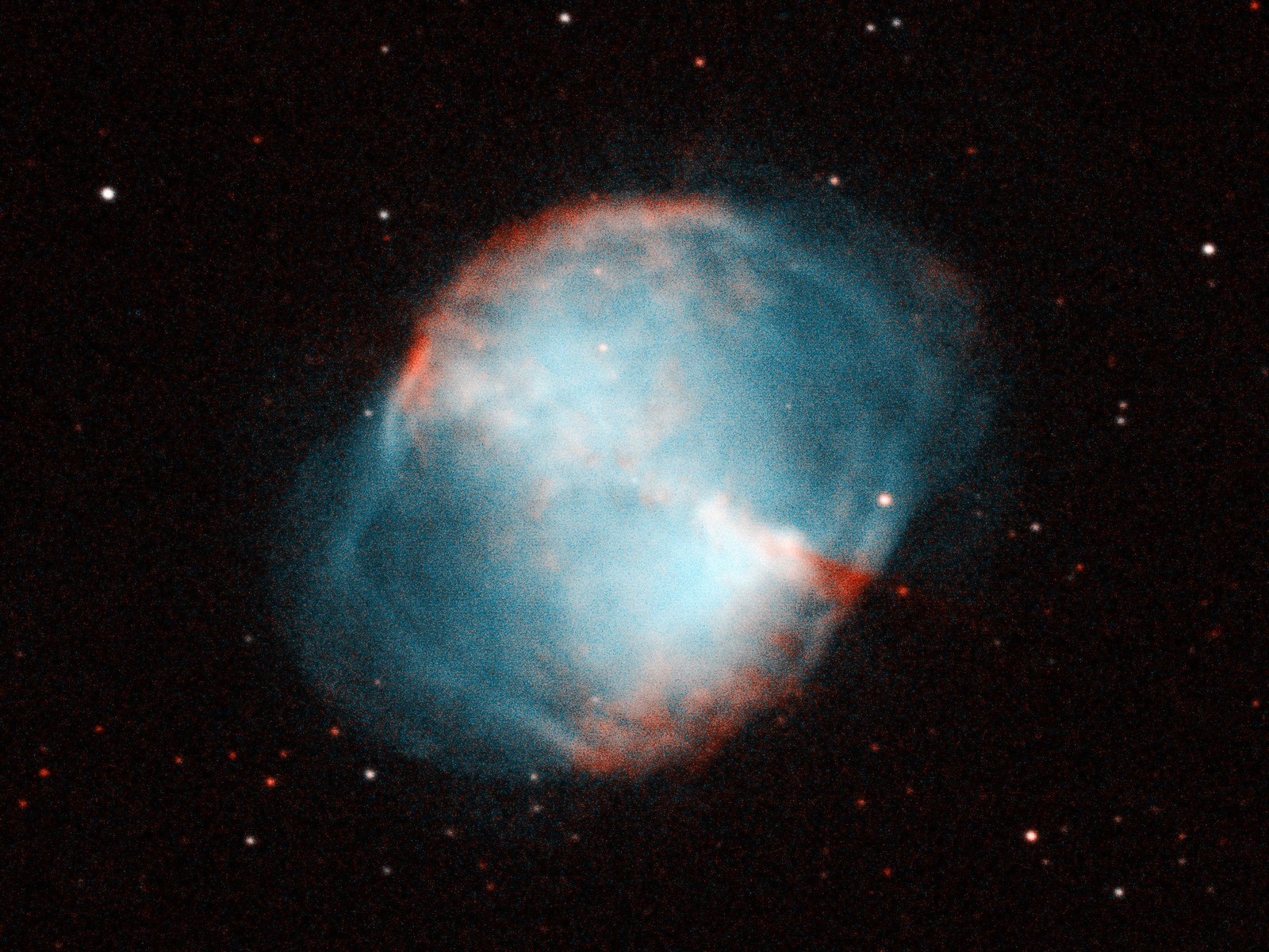 A glowing oval nebula on a dark star field: a bright teal hourglass across the middle, red-orange knots along its upper left and lower right edges, and a fainter blue-grey shell filling out the oval around it.