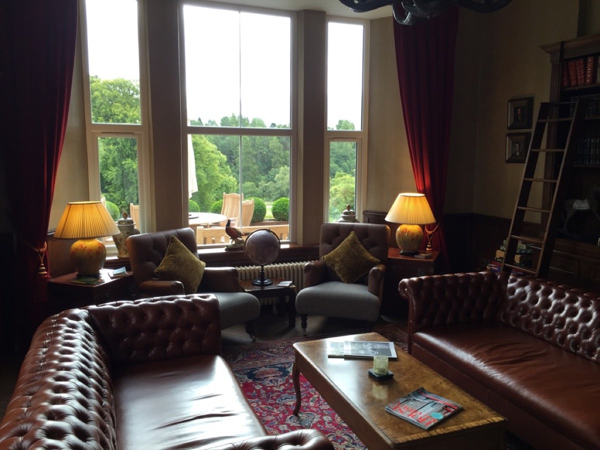 A hotel library with leather Chesterfield sofas, two lamps, a globe, and tall windows onto a garden.